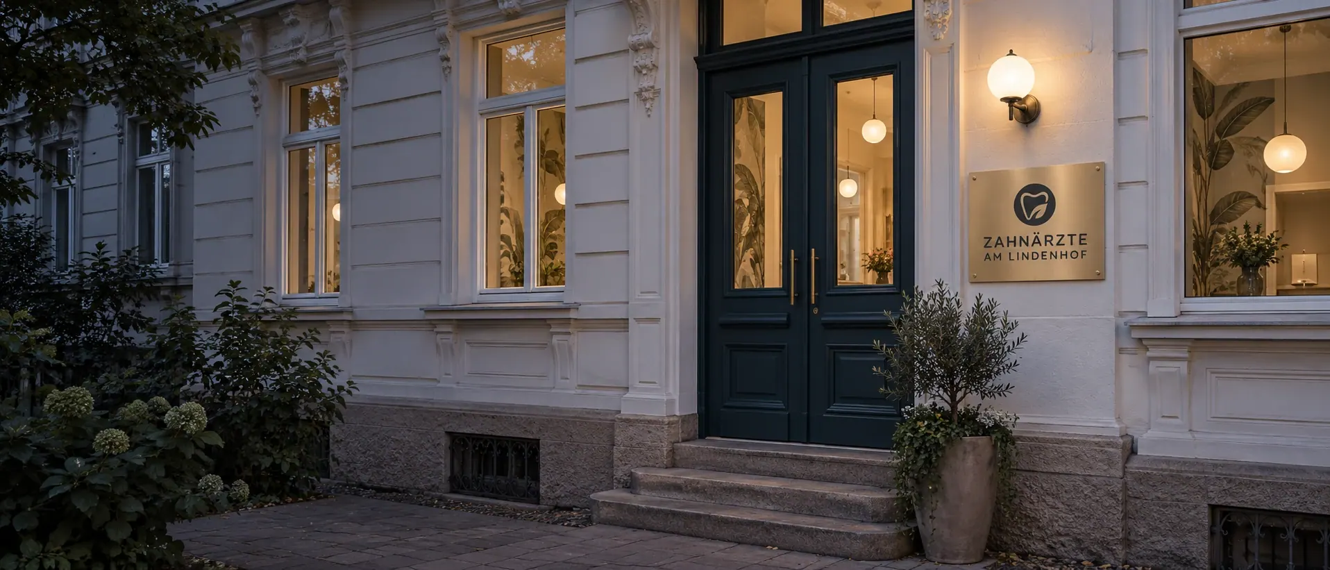 Gründerzeit-Altbau in der Wiehre am Abend: petrolblaue Eingangstür mit Messingschild der Zahnärzte am Lindenhof, warm erleuchtete Fenster.